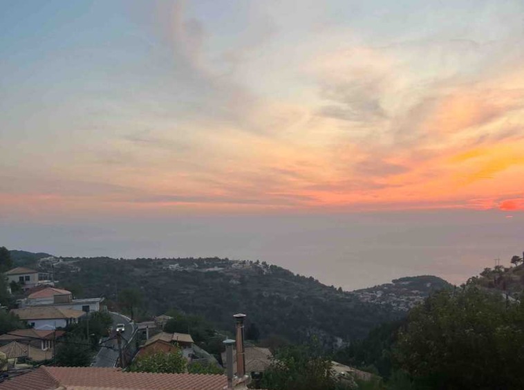 Breathtaking view of a quaint village and serene beach from the Exanthia Stone House, showcasing the property's idyllic location.