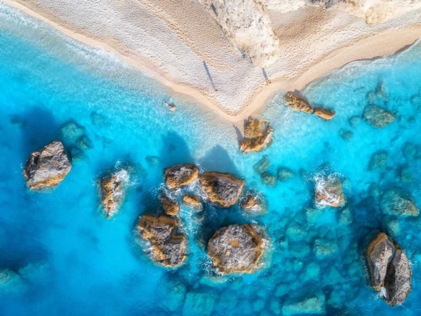Aerial view of beachside property for sale in Lefkada, Greece, with clear boundaries between the sandy beach and lush greenery.