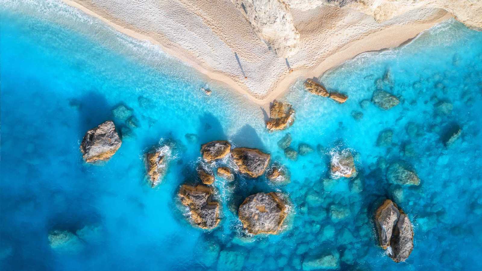 Aerial view of beachside property for sale in Lefkada, Greece, with clear boundaries between the sandy beach and lush greenery.