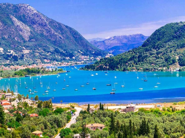 A vibrant panorama of Lefkas with scattered sailboats on the blue waters, surrounded by lush green hills and a clear sky.