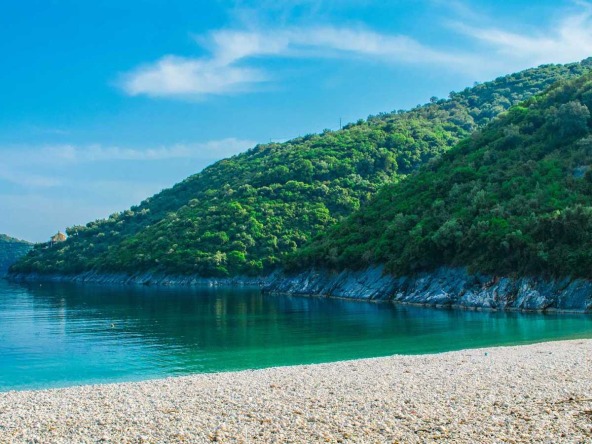 A stunning shot captures the tranquil beauty of the beach in Poros, Lefkada. The clear turquoise waters gently lap against the sandy shore, framed by lush greenery. Ideal plots of land for sale in Poros promise the opportunity to own a piece of this paradise.