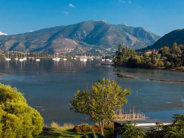 Scenic view of the calm waters and moored sailboats in Geni, Lefkada, with lush green hills and trees under a clear blue sky, find perfect investments with Land for Sale in Geni Lefkada